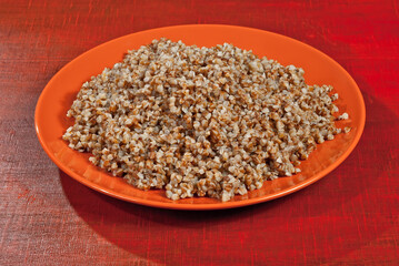 Buckwheat orange plate on a wooden table. Food in utensils on a background of old red plywood.
