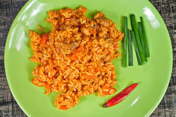 Pilaf with meat, peppers, onions and carrots in a green plate. Rice on a black shabby board.