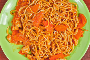 Pasta with carrots in a green plate on a wooden table. Vermicelli with orange sauce on red plywood.