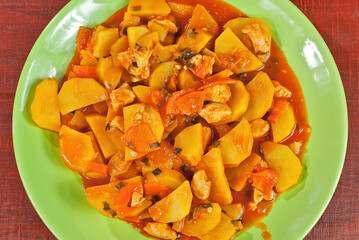 Potatoes in a green plate on a wooden table. Boiled potatoes with orange sauce on a red board.