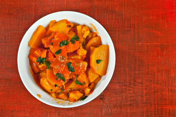 Potatoes in a white plate on a wooden table. Boiled potatoes with orange sauce on a red board. Place for text near the plate. Copy space for design.