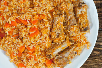 Pilaf with meat and carrots in a green plate. Rice on a brown shabby board.