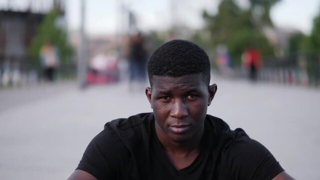 young sad black man sitting on the sidewalk looking at camera - outdoors