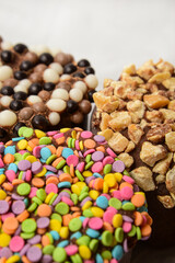 Three marshmallows in chocolate with multi-colored confetti, nuts and waffle topping closeup.