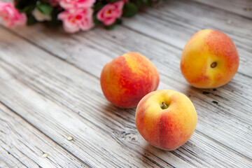 peaches on a light wooden background, flowers are blurry