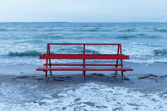 Red bench covered by ice is hit by winter sea. Icy waves of Baltic sea on empty beach. © yegorov_nick