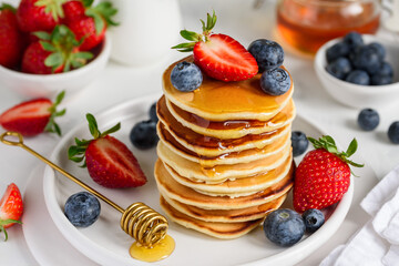 American pancakes with berries and honey on a white plate. Stack of fritters with strawberries and blueberries. Selective focus