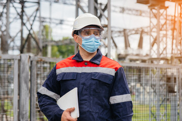 An electrical substation engineer inspects modern high-voltage equipment in a mask at the time of...