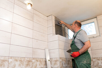 A construction worker applies cement glue to the wall to glue the next ones.