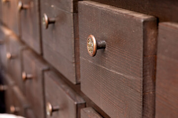 Obraz premium Wooden chest of drawers with small drawers and round brass handles for storing buttons, jewelry, and jewelry. Historic element of an interior