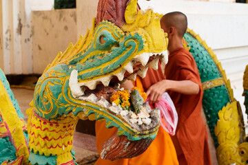 young monk making an offering to a dragon at the entrance of Wat Sisaket, Vientiane, Laos