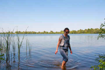 Fototapeta na wymiar Girl in denim overalls goes in the water in the river