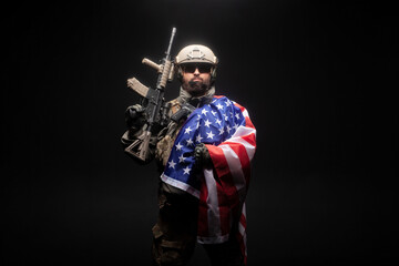 army of america. A soldier in military equipment with a gun holds the USA flag on a black background, American special forces