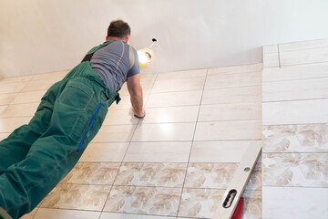 A construction worker applies leveling compound to the ceiling with a stainless steel trowel. Works...