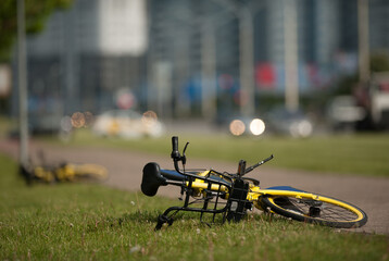 
yellow abandoned bike lies on the grass against the background of the cityscape