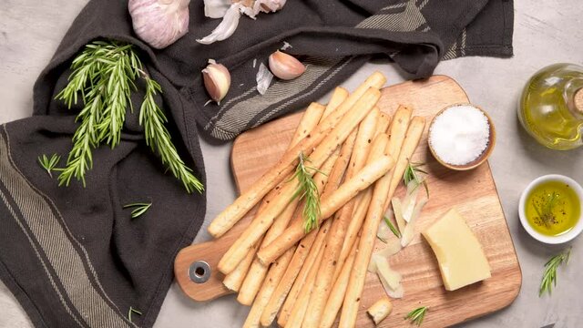 Fresh baked homemade grissini bread sticks in vintage metal grid box with olive oil and rosemary herbs over kitchen counter top.