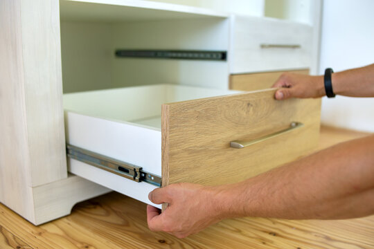 Close up of carpenter hands installing wooden drawer on sliding skids in contemporary cupboard cabinet.