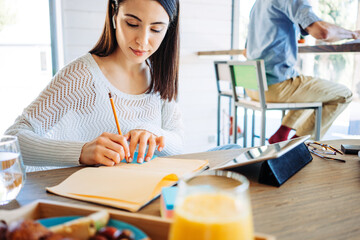 Handsome woman with long hear have online conversation in her own house using tablet computer. Remote workplace. Making marks with pencil, man on background