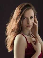 Obraz premium Portrait of a beautiful young girl. The girl stands and gently touches her face with her hands. Dramatic portrait. The light of the sun in the hair.