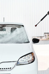 A white car washing with pressurized water at self wash service outdoors at sunny day. Manual car...