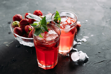 A refreshing summer drink made from strawberries and mint, juice, soda with ice cubes and berry slices, in a beautiful glass with water droplets on a wooden board, dark background with place for text
