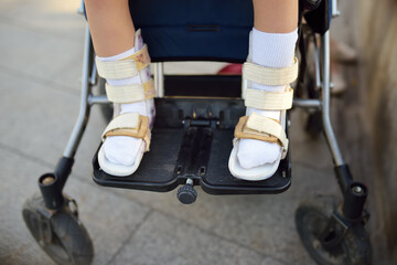 Disabled girl sitting in wheelchair. On her legs orthosis. Child cerebral palsy. Disability....