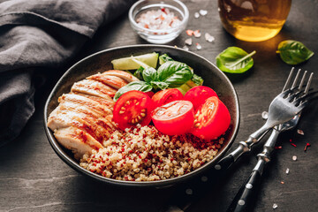 Healthy salad bowl with quinoa, tomatoes, chicken, cucumber and basil on black wooden background. Superfoods.