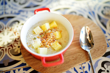 Pudding with fruits, nuts and seeds in red bowl on the table of cafe. Dessert. Healthy eating.