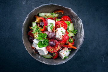 Traditioneller griechischer Bauernsalat mit Tomaten, Oliven und Feta Käse angeboten als Draufsicht in einer rustikalen Modern Design Schale