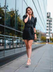 Naklejka premium A young Caucasian businesswoman entering the office to work in a black suit and heels. To the black glass building one spring morning