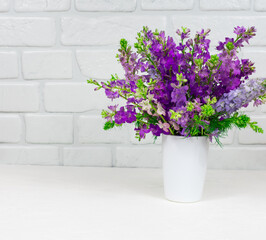 Beautiful bouquet of lilac purple flowers in a white vase on a white background. Mothers Day. Greeting card. Place for an inscription.