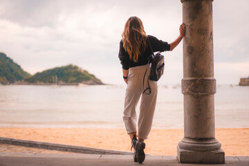 Lifestyle in the city with a blonde girl in white pants and a leather jacket near the beach. Photos...