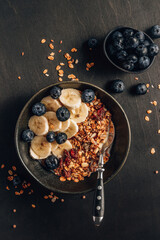 Healthy breakfast concept with homemade granola with banana and blueberries on black wooden background