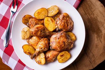 Chicken baked in pieces with potatoes and onion on a white dish.