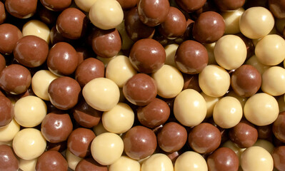 Background made of chocolate hazelnuts covered with milk chocolate and white chocolate. Choco hazelnuts dragee backdrop 