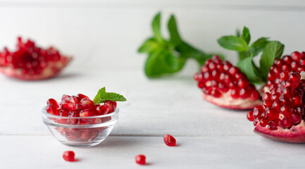 Pomegranate grains in a glass cup, pomegranate and fresh mint on white boards