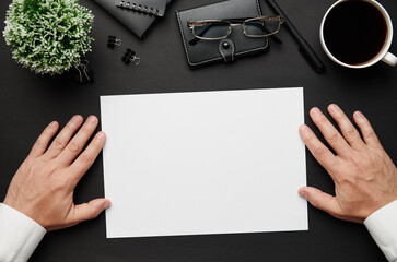 Obraz premium Top view of businessman's hands working. Modern black office desk with notebook, pen and a lot of things. Flat lay table layout. Copy space for text.