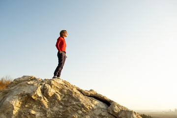 Young woman hiker standing alone on big stone in morning mountains. Female tourist on high rock in wild nature. Tourism, traveling and healthy lifestyle concept.