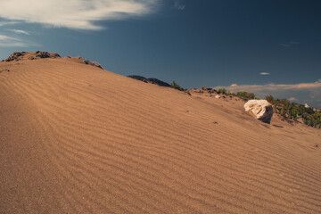 Side shot of a sand dune with line formations and a rock to the right