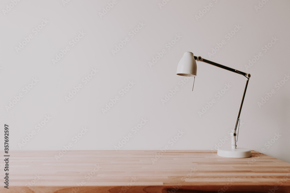 Wall mural white metal lamp on an empty wooden office desk in a room with white wall