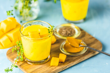 Yellow Indian mango yogurt drink Mango Lassi or smoothie with turmeric and saffron. Healthy probiotic Indian cold summer drink on blue background