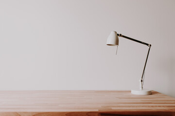 White metal lamp on an empty wooden office desk in a room with white wall