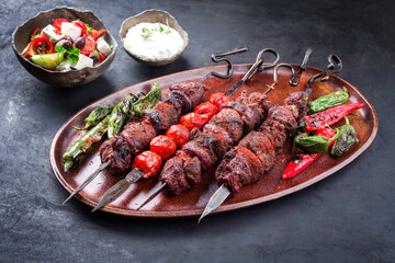 Traditionelles russisches Schaschlik auf einem Grillspieß mit Bauernsalat und Zaziki als close-up auf einem rustikalen Teller