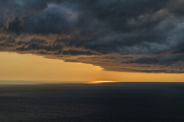 Large dark cloudy formation of a storm over the sea blocking the sun at the background