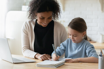 African tutor engaged with schoolgirl help complete tasks seated at table at home. Concept of education kid development, european child homeschooling writing homework with american stepmother concept