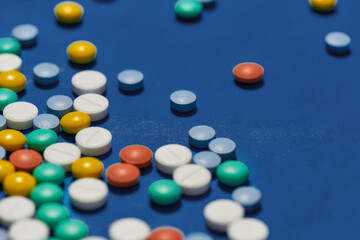 Different colorful pills scattered, lying randomly over blue background. Health care and treatment concept.