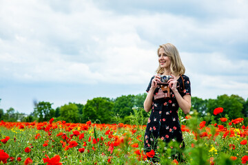 Blonde girl in beautiful dress with vintage camera in poppies field in summer time