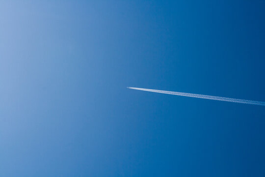 Flying passenger plane on a blue sky with a white smoke trail. Photos of aviation from the ground. Cargo transportation by airplane, air travel. On a sunny clear day.