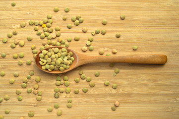 Green lentil grains in wooden spoon, on bamboo cutting board