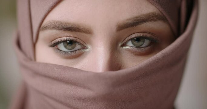 Face with natural make up of attractive muslim gir wearing traditional hijab scarf. Her brown and green eyes looking at camera - beauty, islam concept extreme close up 4k footage